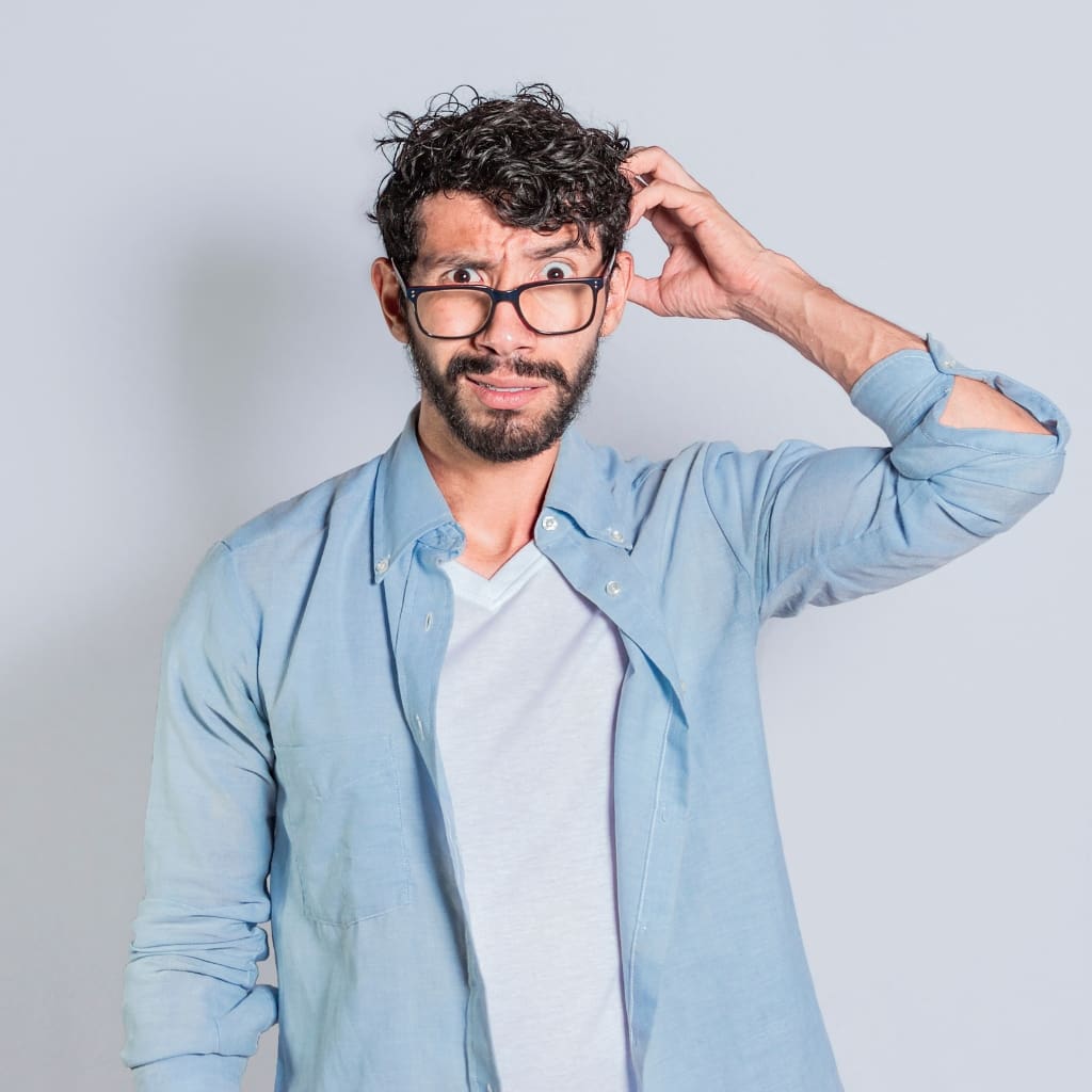 A man with glasses and a beard is holding his hair