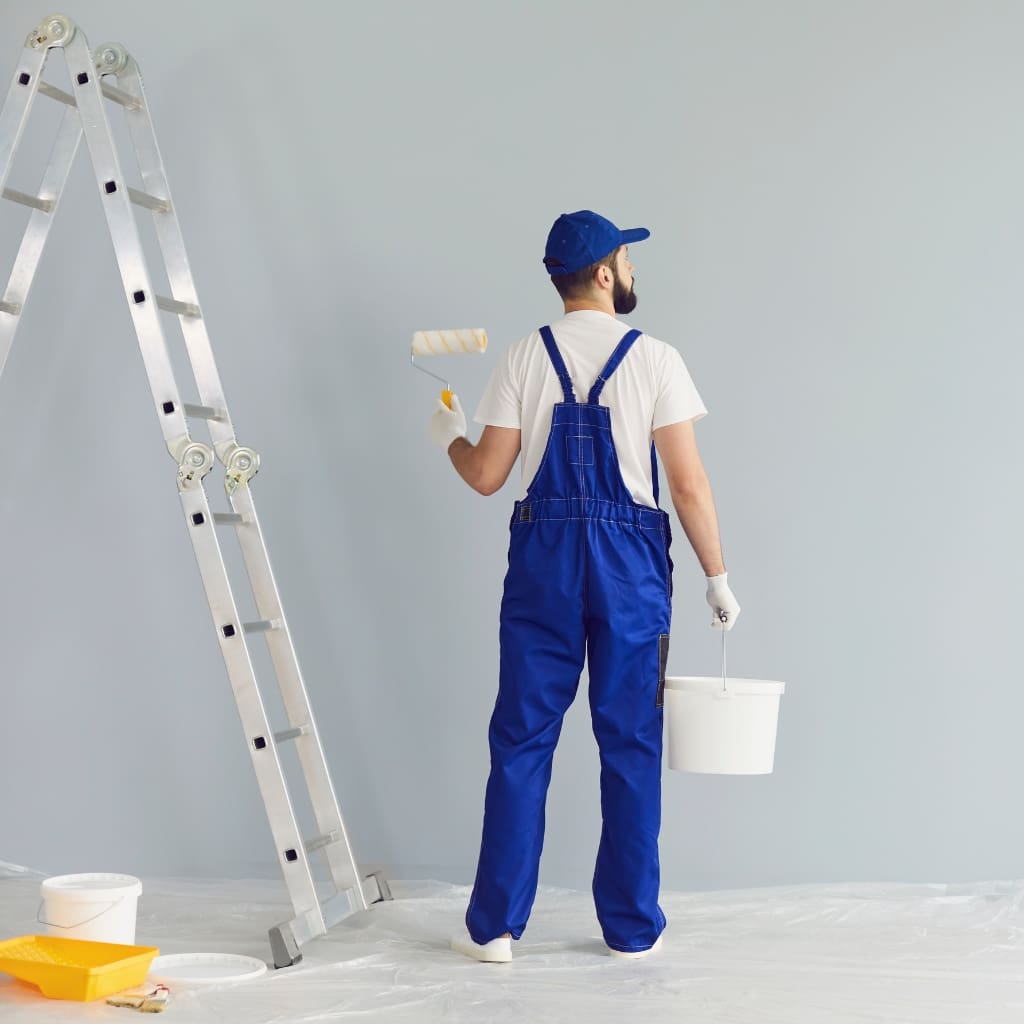 A man in blue overalls holding a paint roller.