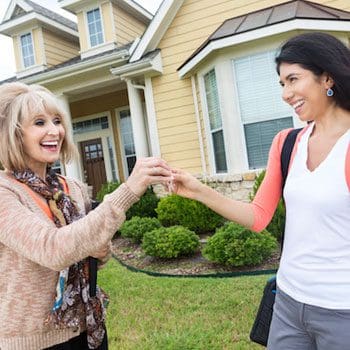 Two women are holding hands in front of a house.