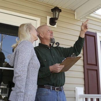 A man and woman standing on the porch of their home.