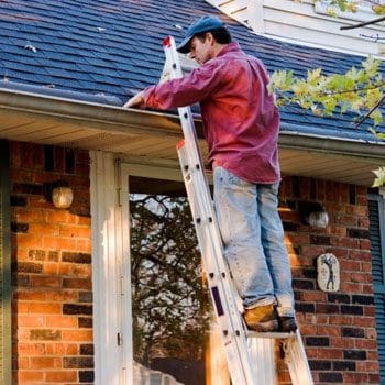 A man on a ladder working on the roof of his house.