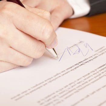 A person is signing papers on top of a table.