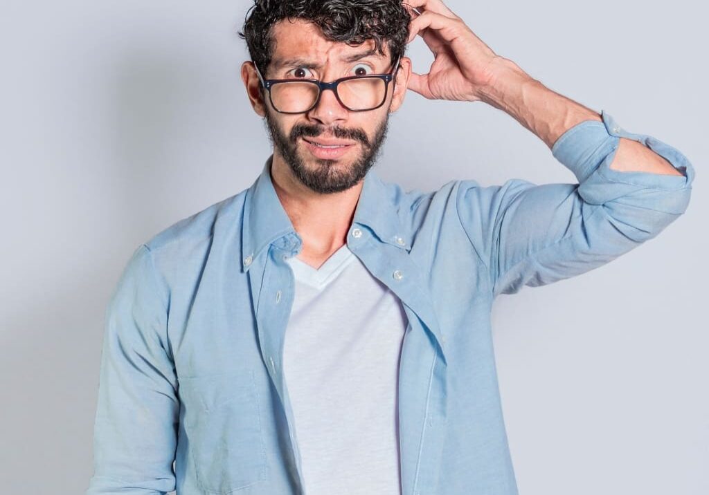 A man with glasses and a beard is holding his hair