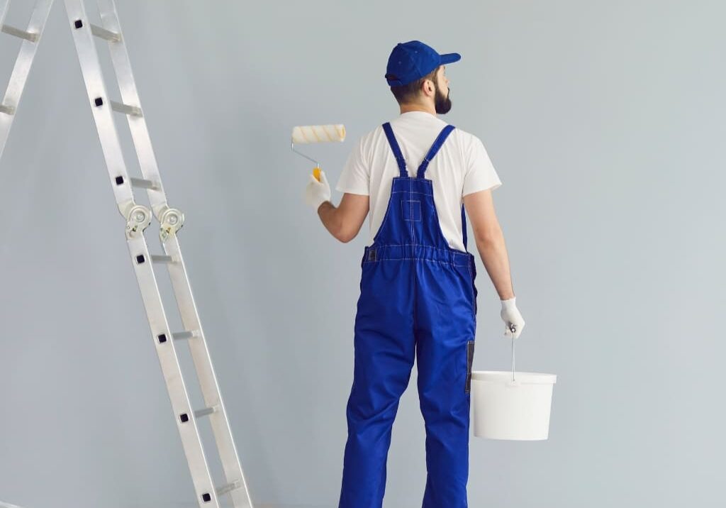 A man in blue overalls holding a paint roller.